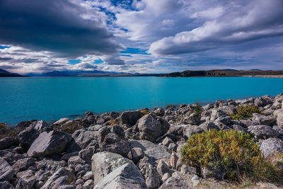 Rocks by lake pukaki against cloudy sky