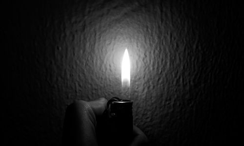 Close-up of hand holding lit candle against wall