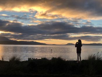 Rear view of girl photographing lake during sunset