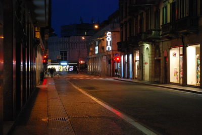 Illuminated road by buildings in city at night