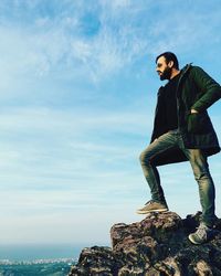 Young man standing on rock against sky