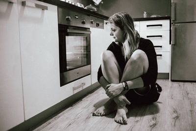 Woman looking at microwave while sitting in kitchen 