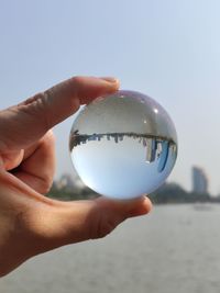 Close-up of hand holding crystal ball against sky