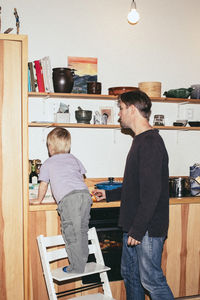 Father near son standing on ladder by kitchen counter at home