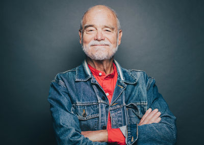 Portrait of smiling senior man with arms crossed against gray background