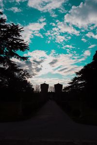 Road amidst silhouette trees and buildings against sky