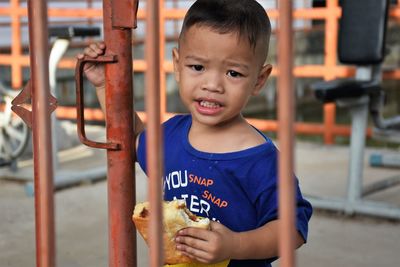 Portrait of boy eating food by gate