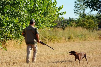 Rear view of hunter standing by dog on land