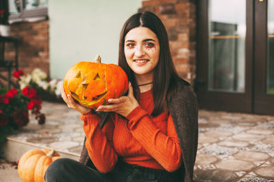 A beautiful girl with dark hair with makeup for the celebration of halloween holds a pumpkin