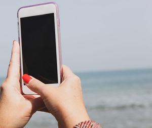 Midsection of woman using mobile phone against sea