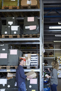 Side view of smiling mature male volunteer standing with female colleague by rack at warehouse