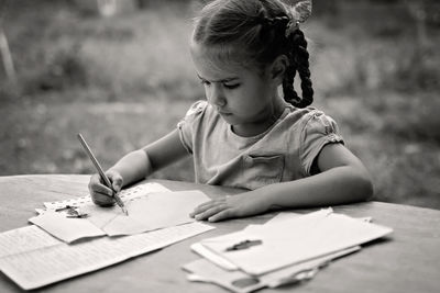 Cute girl drawing on paper while sitting outdoors