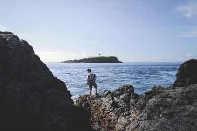 Man standing on rock by sea against sky