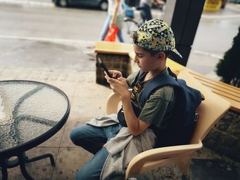 Rear view of boy using mobile phone while sitting on camera