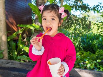 Portrait of smiling girl eating food while standing outdoors