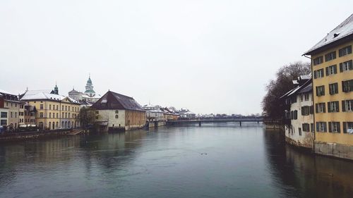 Buildings by river in town against sky