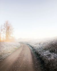 Road amidst field against clear sky during winter