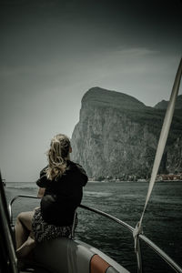 Rear view of woman looking at sea while sitting on boat against mountain