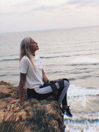 Woman sitting on shore at beach against sky