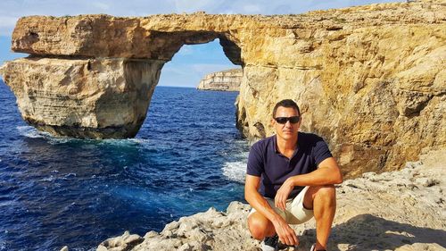 Man crouching against azure window at gozo island