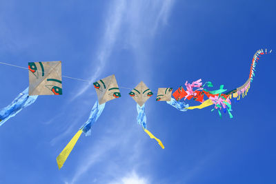 Low angle view of kites flying in blue sky