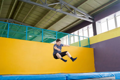 Full length of woman jumping against yellow wall