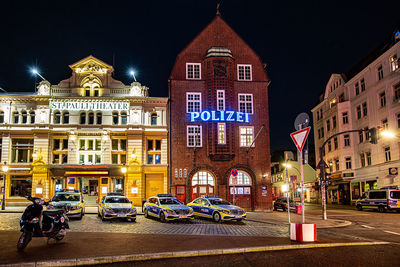 Cars on street against illuminated buildings in city at night