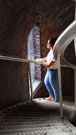 Side view of woman looking through window while standing on staircase