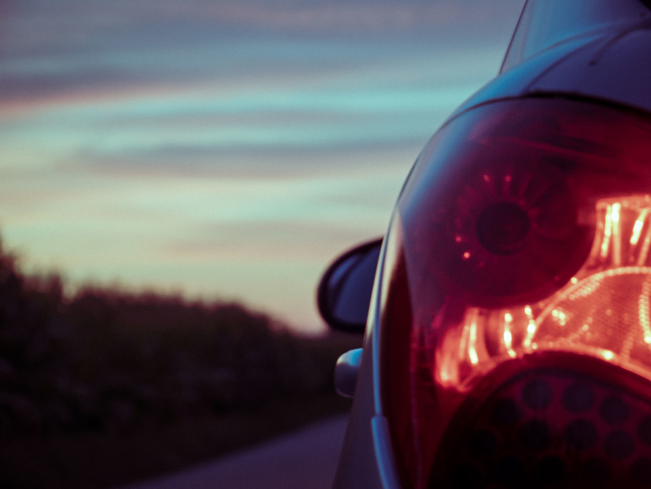 transportation, red, light, car, mode of transportation, vehicle, sky, no people, focus on foreground, motor vehicle, automobile, close-up, road, nature, sign, automotive tail & brake light, dusk, cloud, outdoors, sunset, tail light, land vehicle, screenshot, travel, illuminated