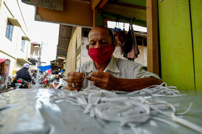 Low angle view of man wearing mask holding textiles on table