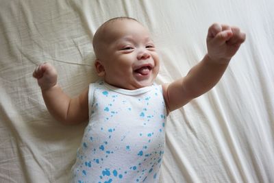 Portrait of cute baby with hand raised lying on bed at home