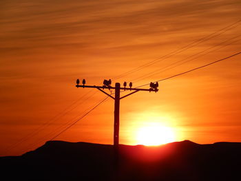 Silhouette telephone pole against sky during sunset