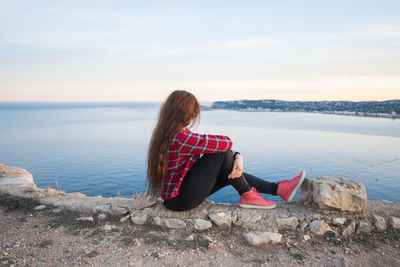 Woman sitting on rock by sea against sky