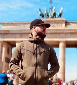 Young man looking away while standing against built structure