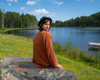 Mature woman full of thoughts wearing hat and sweater sitting in front of karelia lake