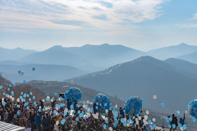 People with helium balloons against sky on sunny day