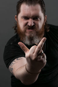 Mid adult man gesturing obscene gesture while sitting against black background