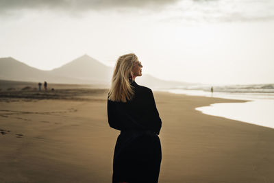 Rear view of woman standing at beach against sky