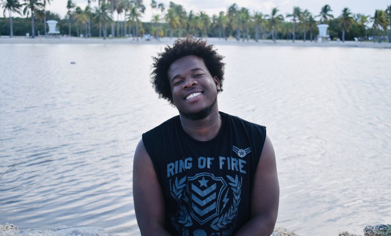 PORTRAIT OF SMILING YOUNG MAN STANDING AT BEACH
