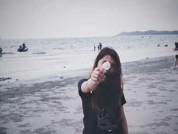 Mature woman holding seashell while standing at beach against clear sky during sunset