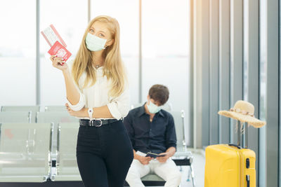 Portrait of young traveler in protective mask holds passport during affected by flight delay