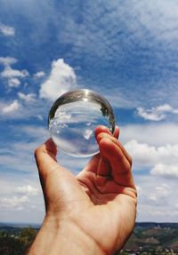 Cropped hand holding crystal ball against sky