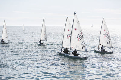 People sailing on sailboat in sea against sky