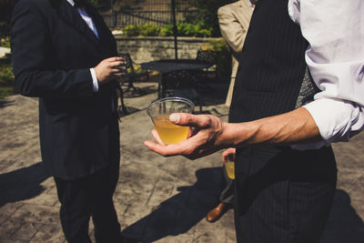 Midsection of men holding drink in glass while standing outdoors