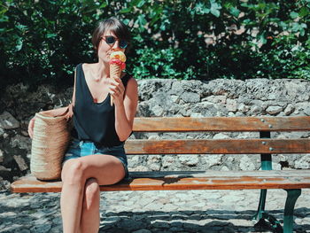 Woman eating ice cream while sitting on bench during sunny day