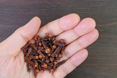 Heap of dried cloves in hand on black wooden backdrop