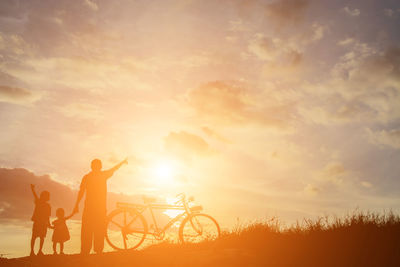 Silhouette people riding bicycle against sky during sunset