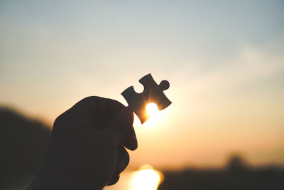 Silhouette person holding sun during sunset