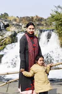 A young woman with her daughter standing near to a waterfall