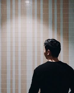 Rear view of man standing against tiled wall